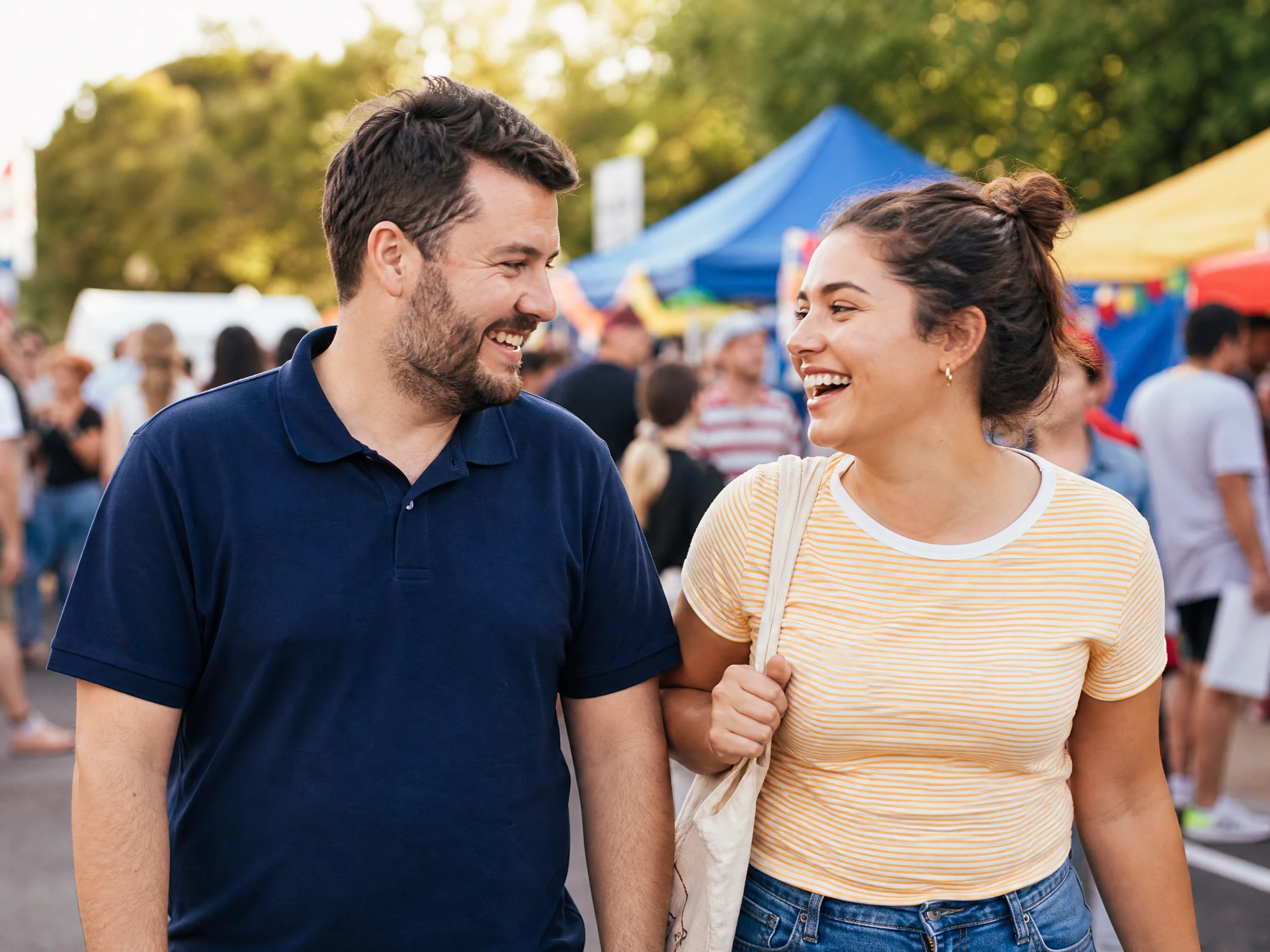 Support worker in navy polo shirt laughing with a young adult participant at a vibrant outdoor community event